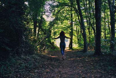 Rear view of woman walking on road in forest