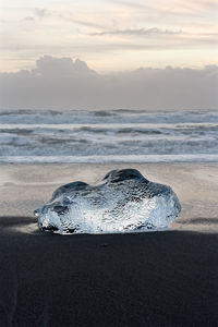 Round ice block in blue shades on a beach with strong surf, iceland