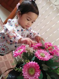 High angle view of cute girl touching artificial flowers in vase at home