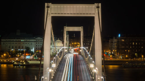 Light trails on bridge in city against sky at night