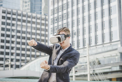 Businessman looking through virtual reality simulator while standing against building