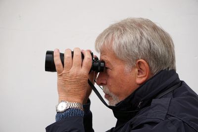 Side view of man looking through binoculars against white background