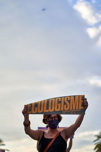 Man holding camera while standing against sky