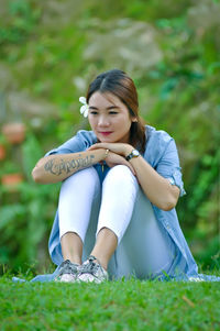 Thoughtful young woman sitting on grassy land in park