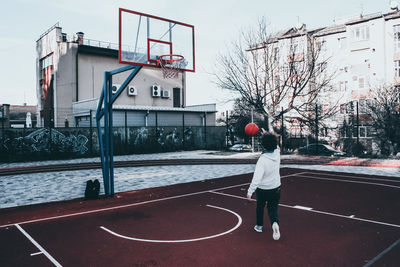 Rear view of man with basketball hoop against sky