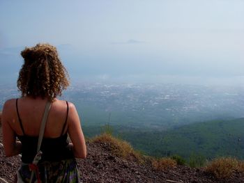 Woman with curly hair standing on cliff against mountains