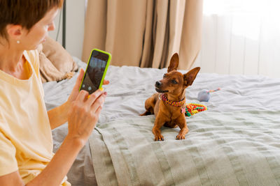 Mature woman with a phone in her hand with a pygmy pinscher in the bedroom