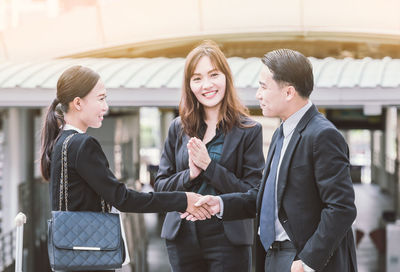 Businesswoman clapping while colleagues giving handshake against building