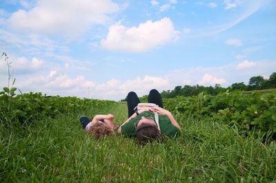 Mother and daughter lying on grass against sky