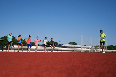 Group of women practice pre-workout stretching with their young traine
