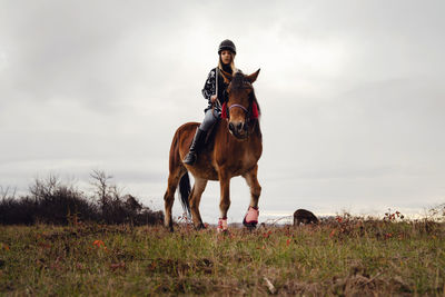 Woman riding horse on field against sky