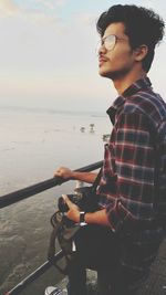 Young man sitting on sea shore against sky