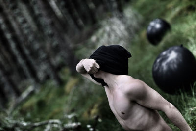 Shirtless man removing t-shirt at forest