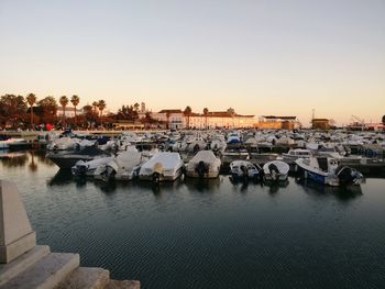 Boats moored in harbor at sunset