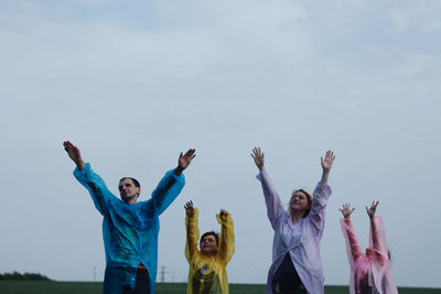 Happy family with arms raised standing on field against sky