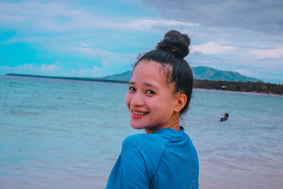 Portrait of young woman standing at beach against sky