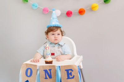 Cute boy sitting with cake by wall