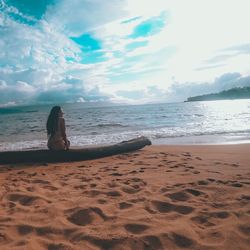 Woman sitting on shore at beach against sky