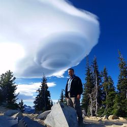 Low angle view of man standing by rocks against cloudy sky