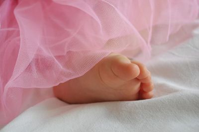 Low section of baby girl in pink dress on bed