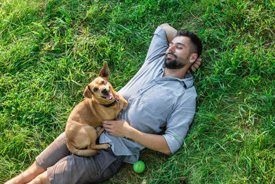 Attractive european man is resting on grass with his cute little dog on a summer sunny day.