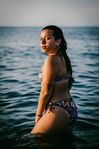 Young woman in bikini standing by sea against sky