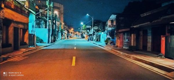 Empty road along illuminated buildings at night