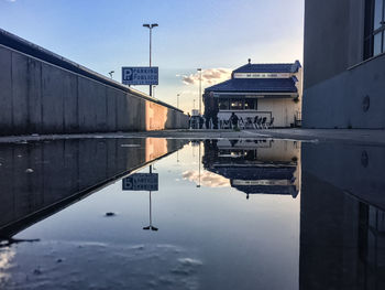 Reflection of bridge in puddle against sky