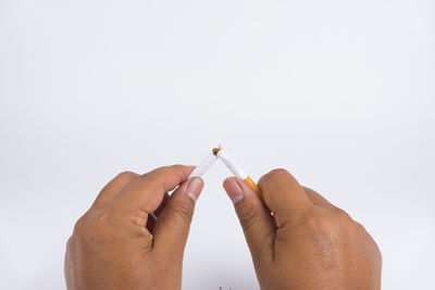 Close-up of hand holding cigarette over white background