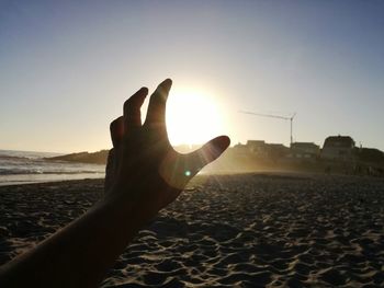 Close-up of hand on sand at beach against sky