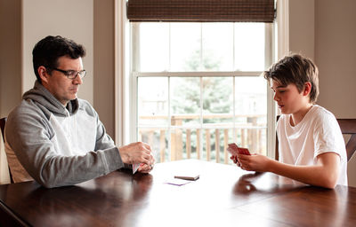 Adolescent boy and his father playing cards at the table together.