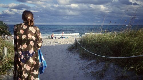 Rear view of teenager girl looking at sea shore against sky