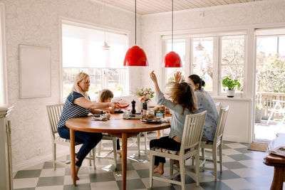 Mothers having breakfast with daughters while sitting at dining table in house