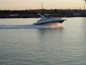 Boat in river against sky during sunset