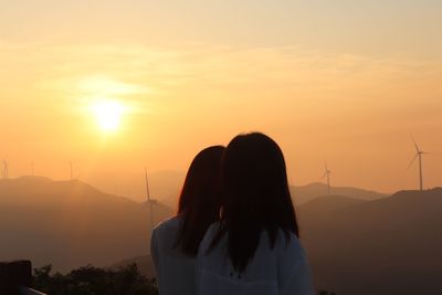 Rear view of women standing against orange sky