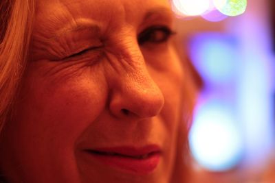 Close-up portrait of mature woman winking in illuminated room
