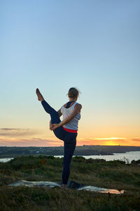 Full length of young woman exercising on field against clear sky