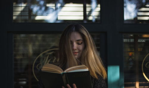 Close-up of young woman reading book against built structure