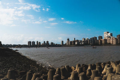 View of city at waterfront against cloudy sky