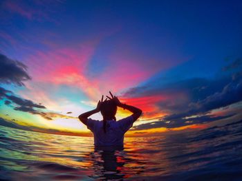 Silhouette woman in sea against sky during sunset