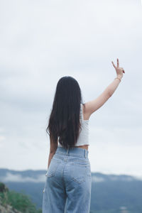 Rear view of woman with arms raised standing against sky