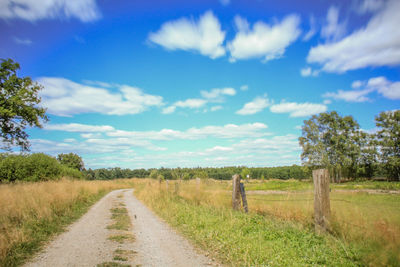 Dirt road amidst field against sky