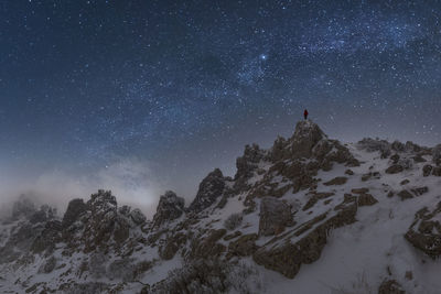 Traveler with glowing flashlight standing on cliff of mountain range in picos de europa national park under dark starry night sky