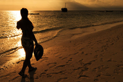 Silhouette woman on beach against sky during sunset