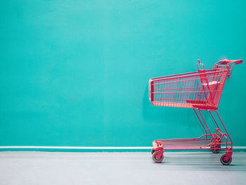 Empty shopping cart against turquoise colored wall