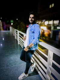 Portrait of young man standing against railing at night