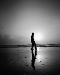 Silhouette man and child walking on beach against clear sky