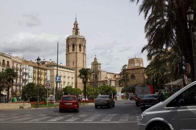 Vehicles on road by buildings in city against sky