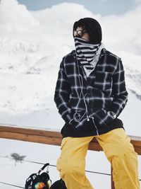 Low angle view of man sitting on railing outside snow against sky