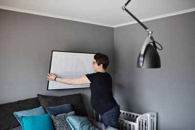 Pregnant female arranging paintings on wall in bedroom at home